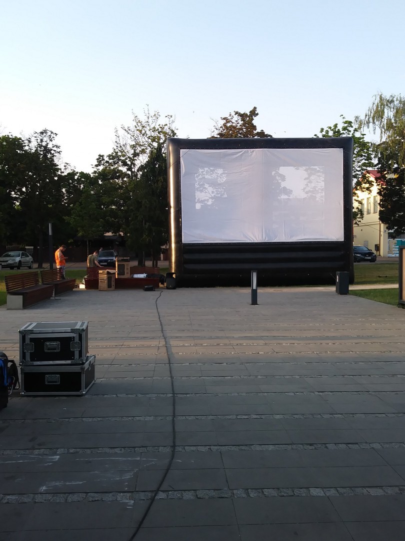Na zdjęciu widać duży ekran kinowy rozstawiony na wyłożonym kostką placu