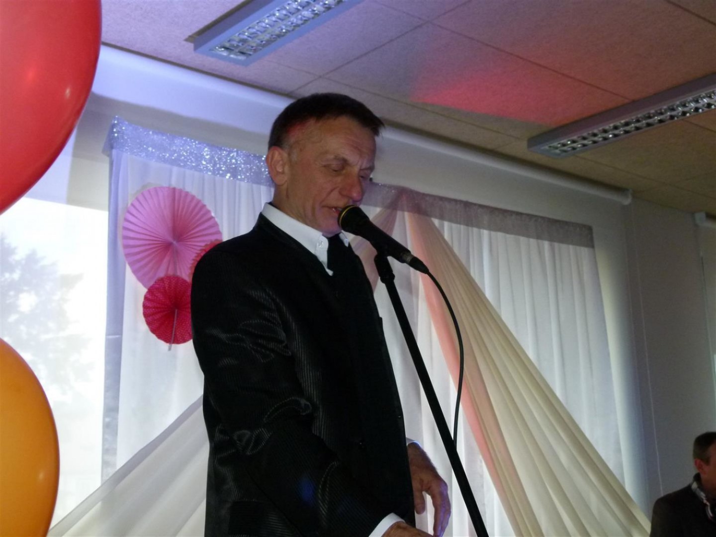 Na zdjęciu widać aktora Krzysztofa Tyńca w garniturze, śpiewającego do mikrofonu