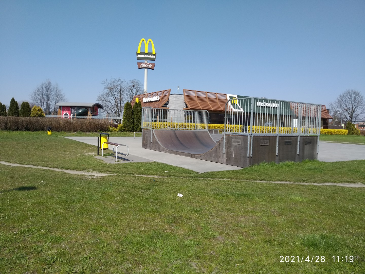 Na zdjęciu widać betonową minirampę skejtparku, a za nią żółte logo makdonalda