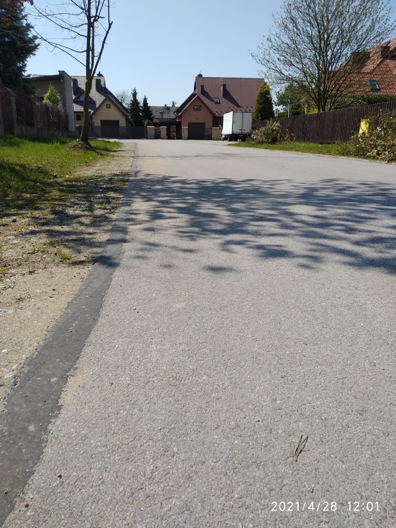 Na zdjęciu widać asfaltową uliczkę, domy i drzewa